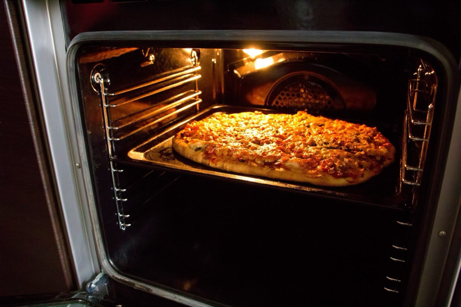 A pizza baking inside a modern electric built-in oven