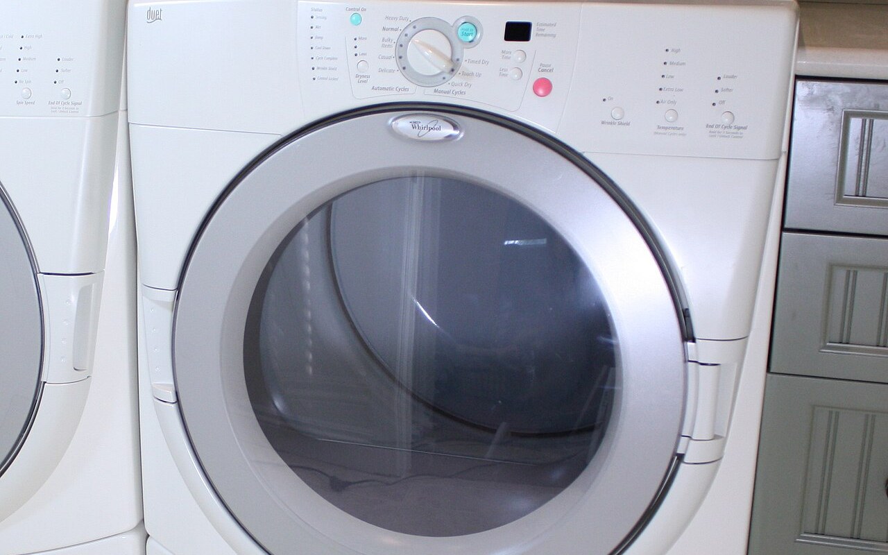 A white front-loading tumble dryer with its control panel and round door visible in a home laundry room