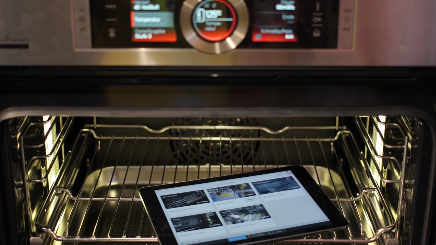 A Bosch connected oven with a digital control panel, shown with a tablet running the Home Connect app inside the oven cavity.
