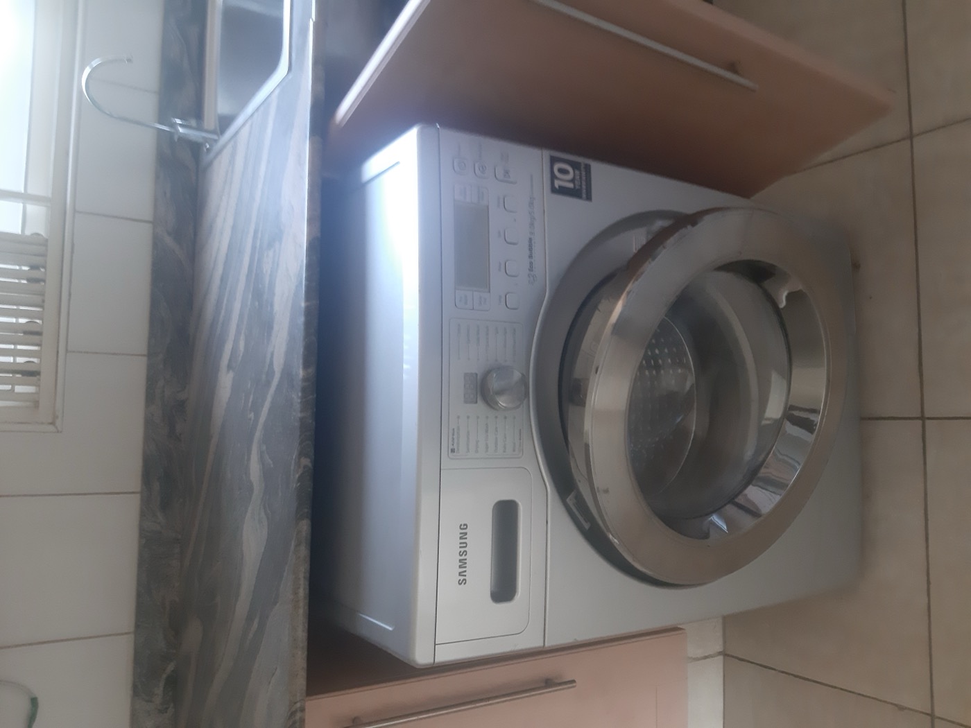 A modern silver Samsung front-load washing machine installed under a kitchen worktop.